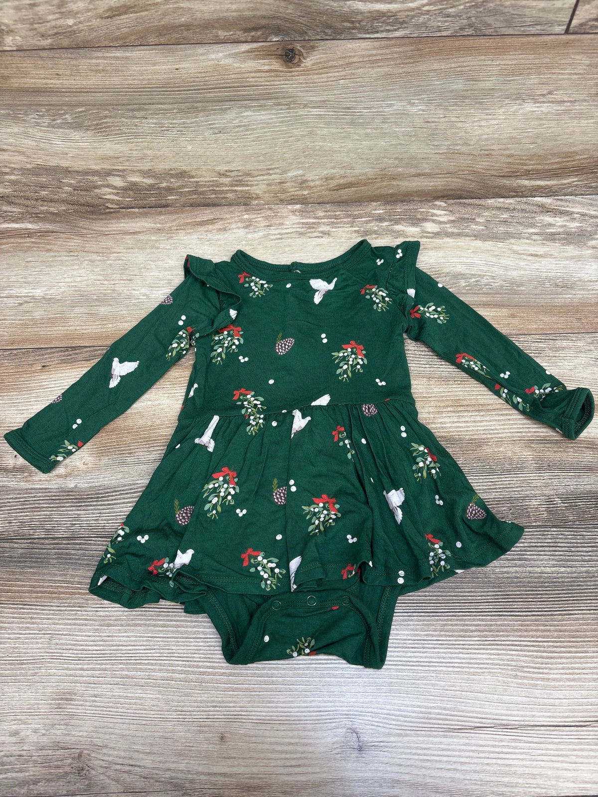 Front view of Kyte Baby Mistletoe Twirl Bodysuit Dress in green with long sleeves, ruffled skirt, and attached bodysuit on wood
