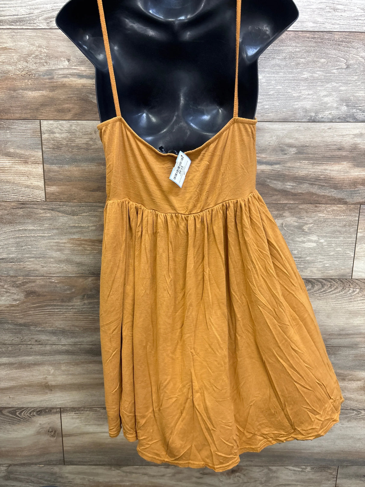 Front of Boohoo mustard yellow maternity sleeveless dress with spaghetti straps and gathered empire waist on wood background