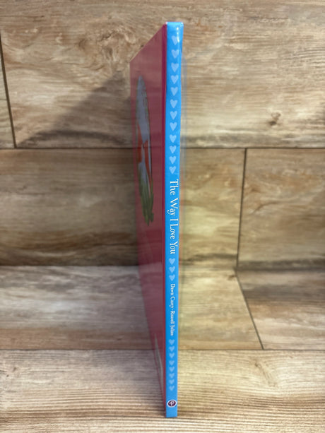 Side view of The Way I Love You hardcover book showcasing blue heart-patterned spine and vertical title with wooden shelf background