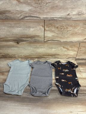 Three baby onesies: striped, navy striped, and black construction vehicle print on wood floor