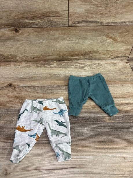 Top view of Child Of Mine newborn pants showcasing solid green and dinosaur print pairs on a wood floor