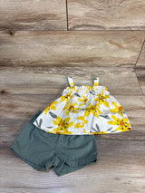 Flat lay of baby two-piece set: white button-front top with yellow floral print, olive-green shorts on wood background