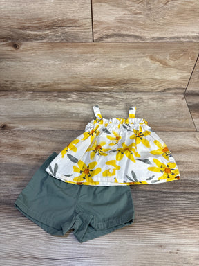 Flat lay of baby two-piece set: white button-front top with yellow floral print, olive-green shorts on wood background