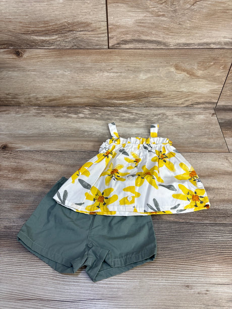 Flat lay of baby two-piece set: white button-front top with yellow floral print, olive-green shorts on wood background