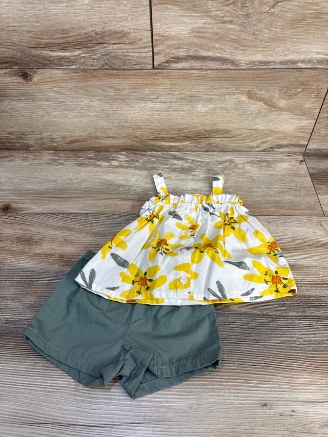 Flat lay of baby two-piece set: white button-front top with yellow floral print, olive-green shorts on wood background