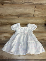 White baby dress with pastel stripes, lace trim, and puffed sleeves on wood floor