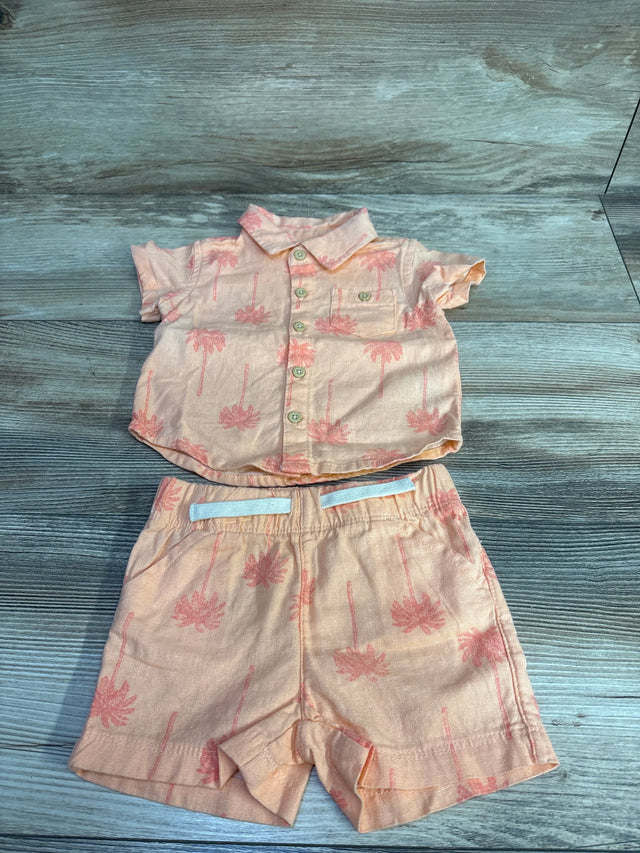 Flat lay of coral newborn two-piece button-up shirt and elastic-waist shorts with pink palm tree print on wood background