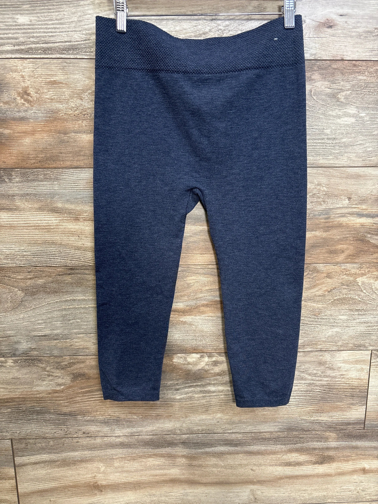 Front view of blue maternity leggings showing textured high waistband and ankle-length legs on wood plank background