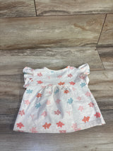 Flat lay of pink Calvin Klein toddler flutter sleeve shirt showcasing ruffled cap sleeves and pastel flower print on wood floor background