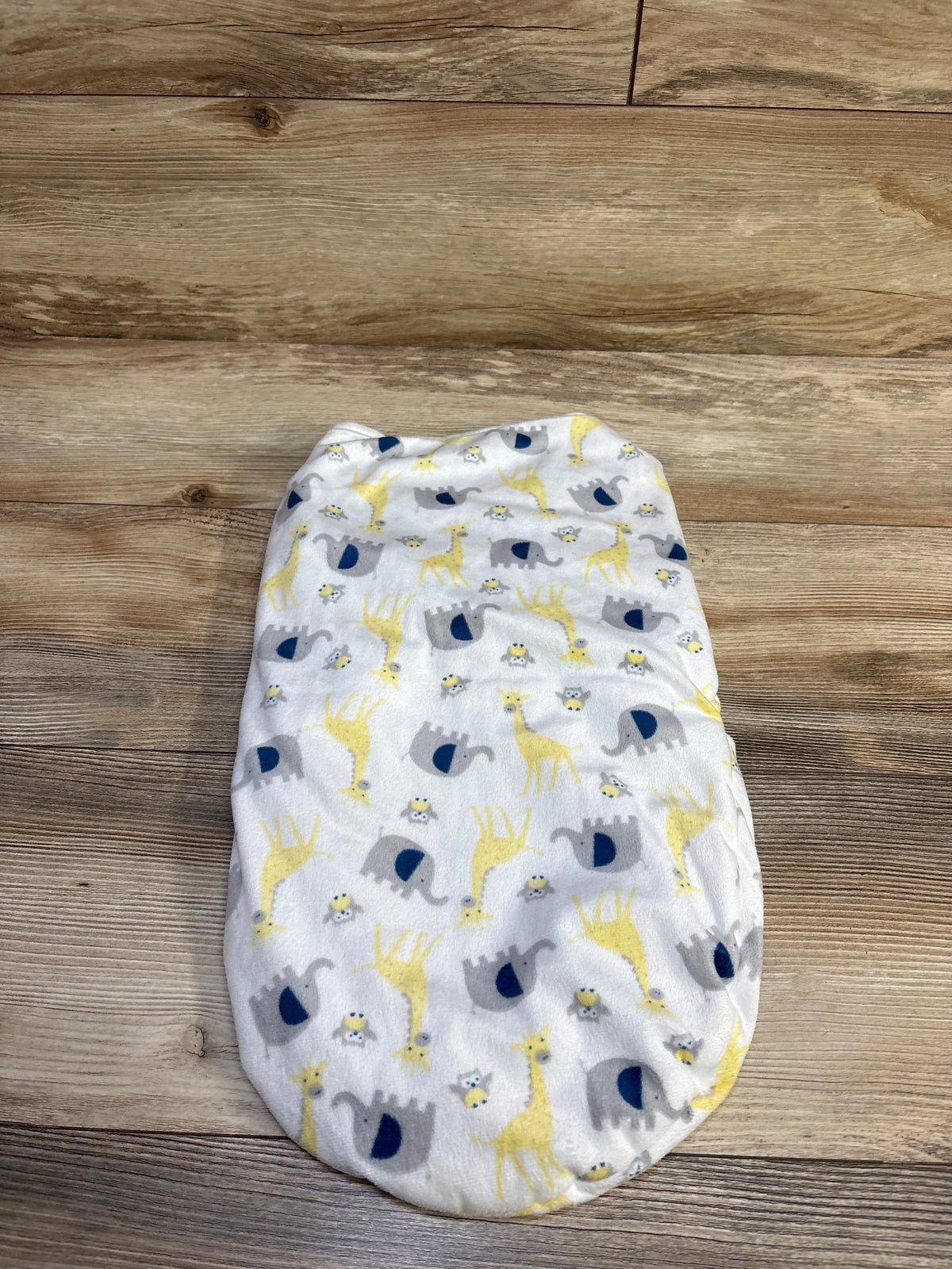 Top view of Petite L’amour plush swaddle wrap in white, showcasing an elephant and giraffe pattern with a wood floor background