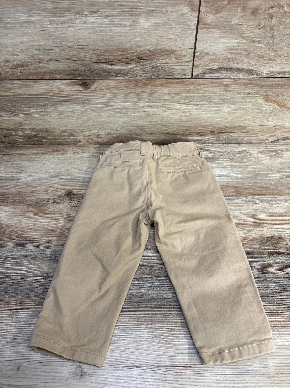 Back view of Baby Gap slim chino pants in khaki, size 2T, showing elasticized waist and back welt pockets on wood floor
