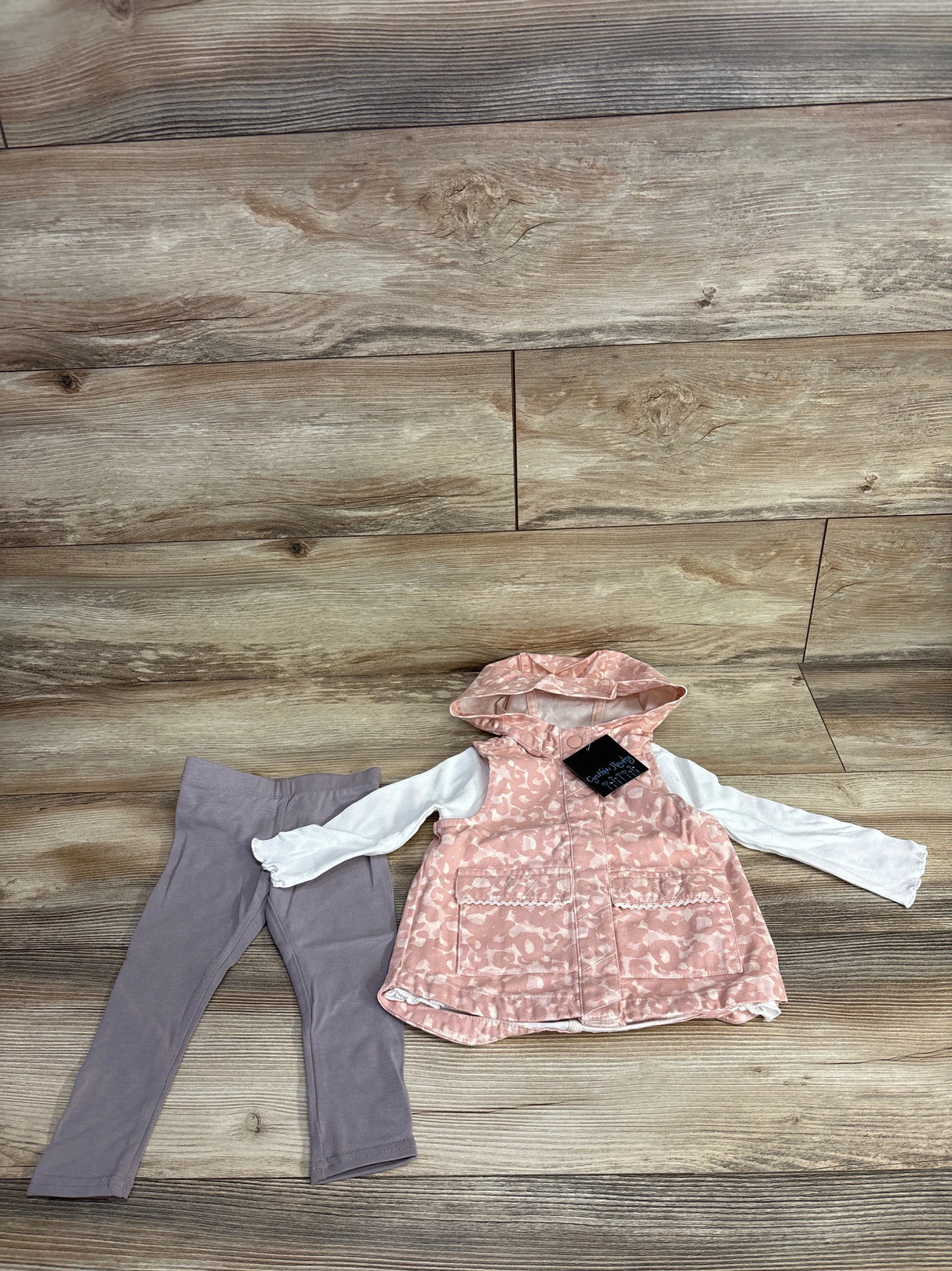 Toddler outfit with pink leopard print hooded vest and long sleeve white shirt paired with gray leggings on wood floor
