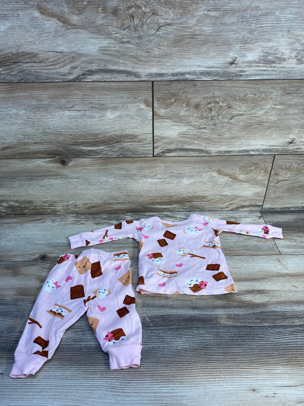 Flat lay of pink 2-piece baby pajama set with smores print, long-sleeve top and elastic-waist pants on wood backdrop