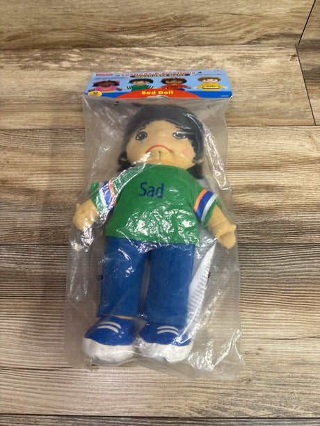 Front view of Feelings and Emotions Sad Doll in clear packaging wearing a green shirt labeled Sad and blue pants