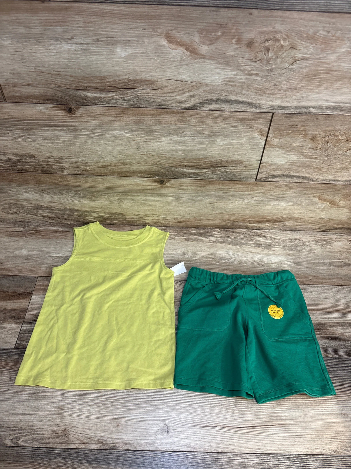 Kids yellow sleeveless top and green shorts set on wood background