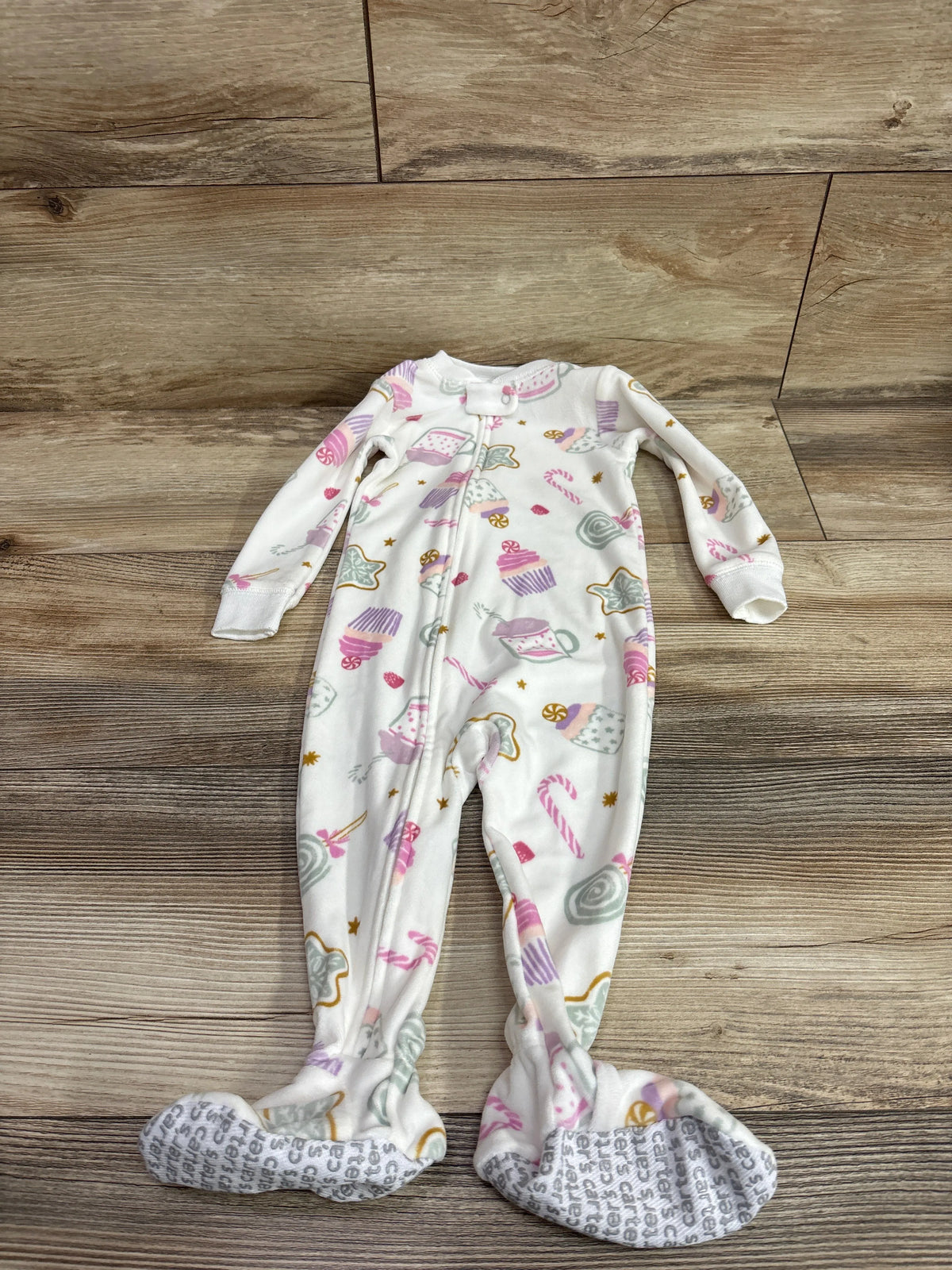 Front view of white Just One You blanket sleeper with pastel candy and cupcake print, zipper, and footed legs on wood flooring