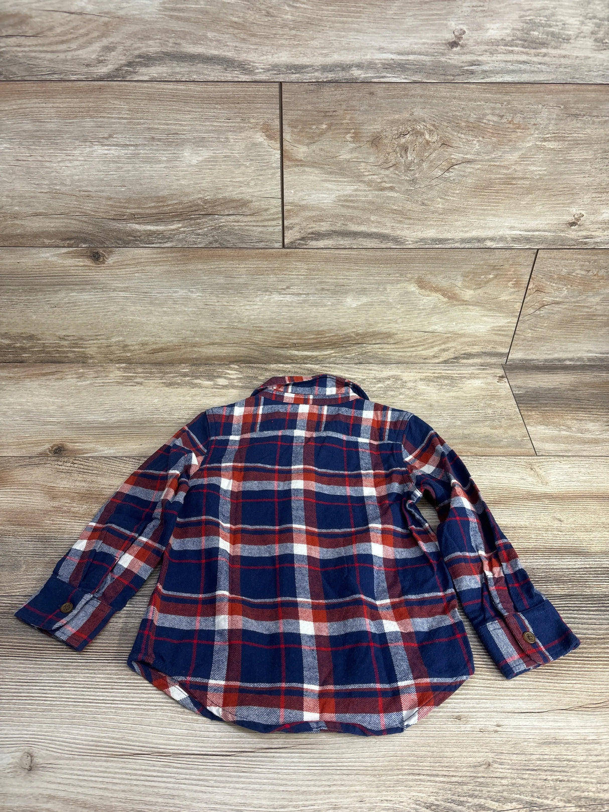 Children's long sleeve blue and red plaid flannel shirt laid flat on wood floor
