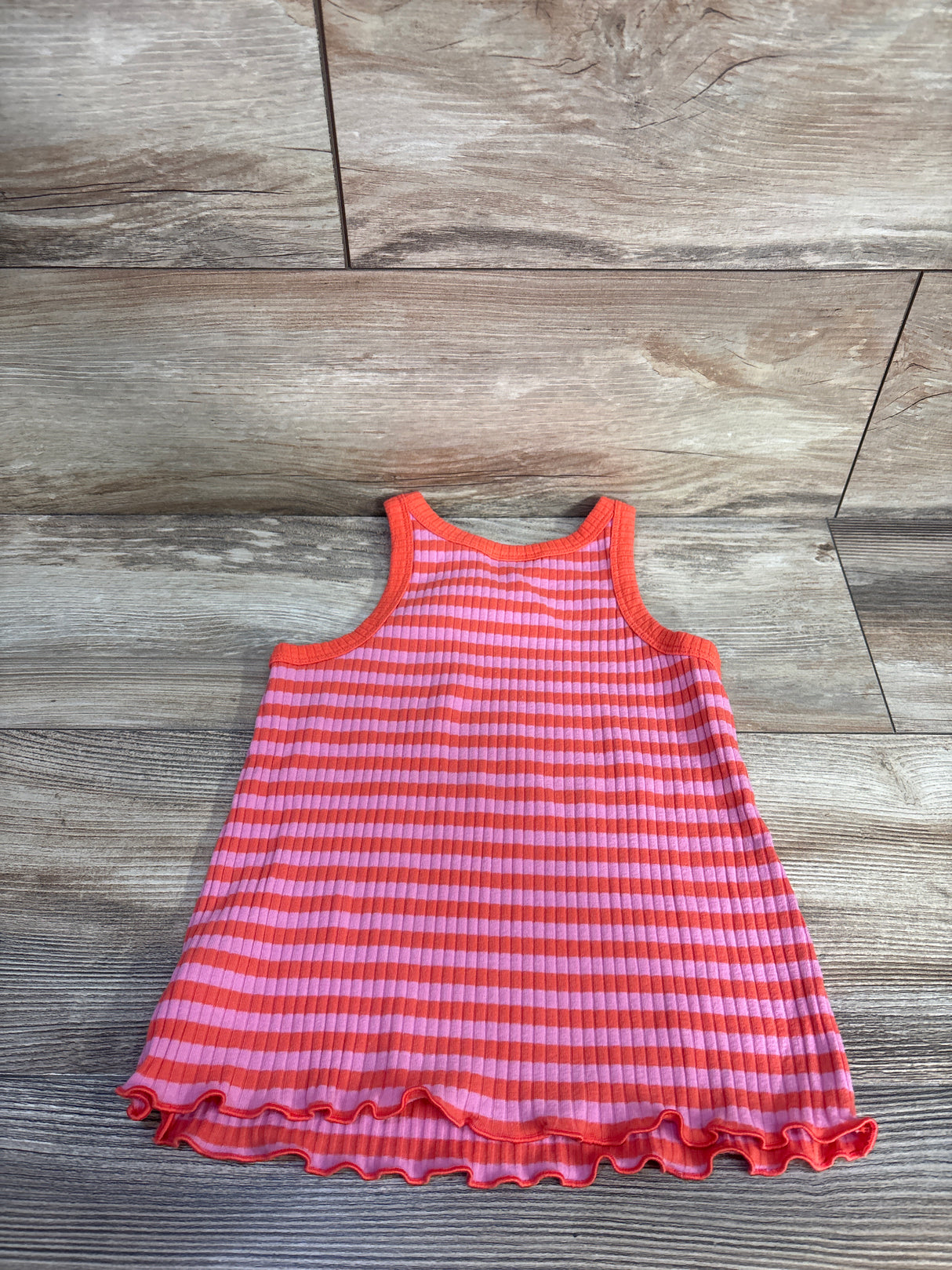Flat lay of Cat & Jack girls' ribbed striped tank top in pink and orange with lettuce-hem ruffle on wood background