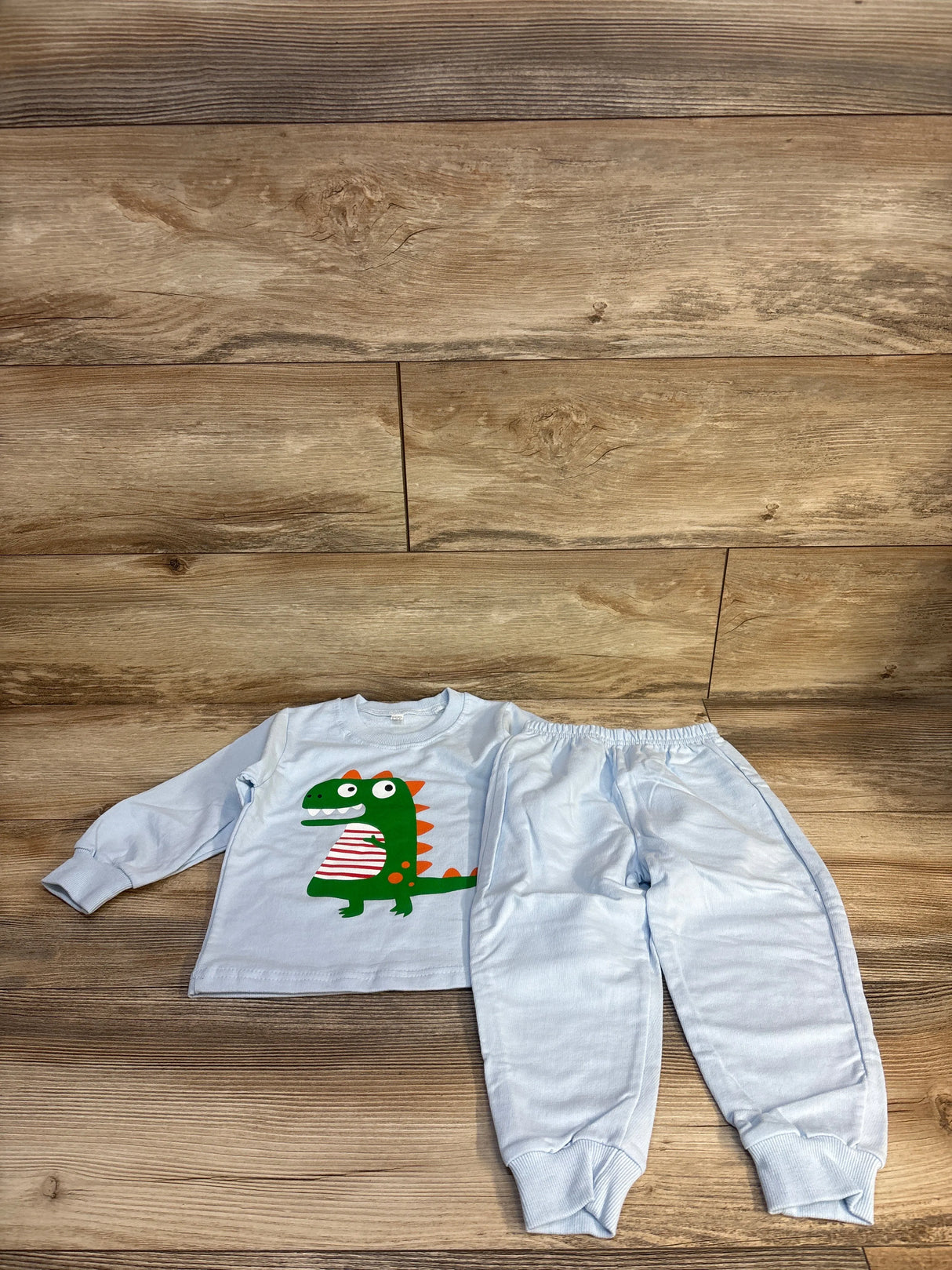 Light blue kids pajama set with green dinosaur graphic, long sleeve top and matching pants on wood floor