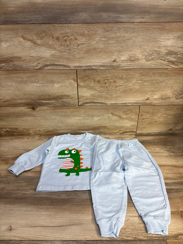 Light blue kids pajama set with green dinosaur graphic, long sleeve top and matching pants on wood floor