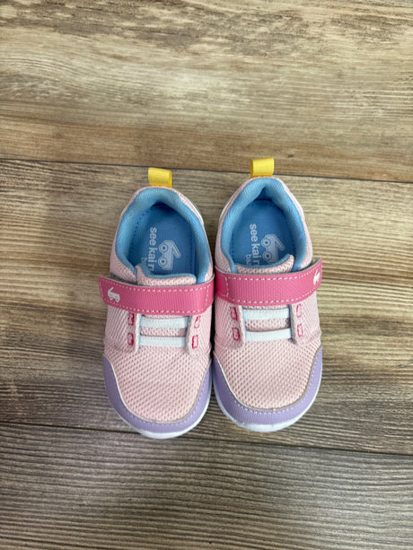 Top view of See Kai Run Basics Stryker sneakers showcasing pink mesh uppers, lavender trim, blue lining, and yellow heel tabs on wood