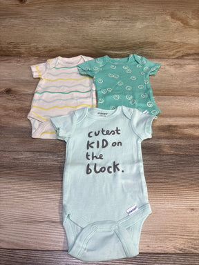 Top-down of three Onesies bodysuits: mint with text cutest KID on the block, teal smiley print, and white striped on wood