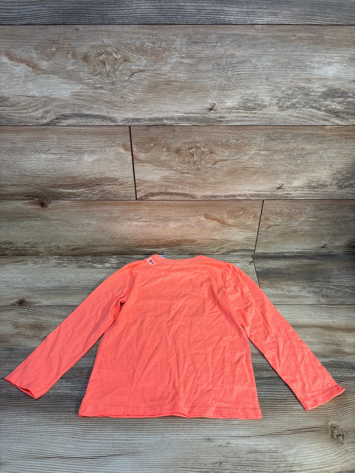 Coral long sleeve kids shirt laid flat on wood floor background, gently used children's clothing