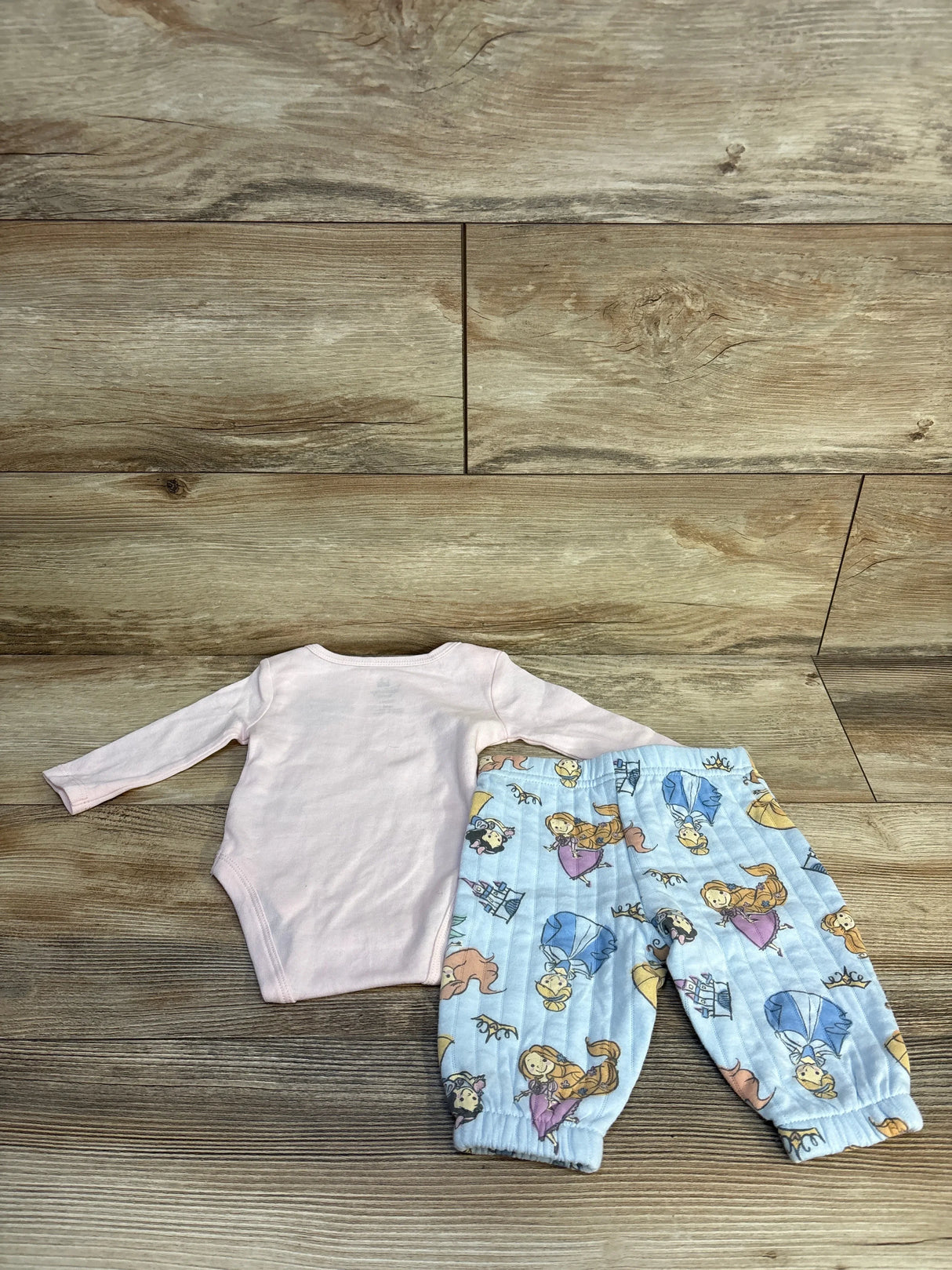Pink baby onesie with blue princess print pants, kids clothing set on wood floor