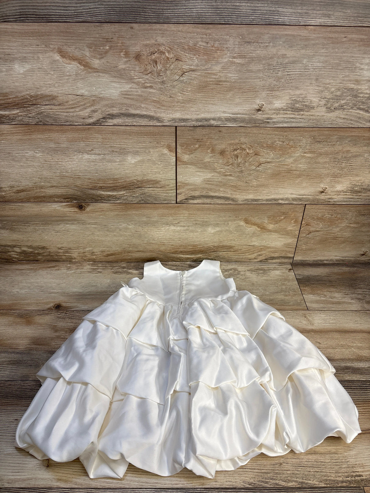 White ruffled baby dress with layered satin skirt on wooden floor