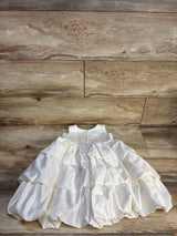 White ruffled baby dress with layered satin skirt on wooden floor