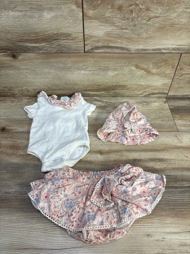 Flat lay of 3-piece baby set: white bodysuit with ruffle collar, pink floral bloomers and matching bonnet on wood background