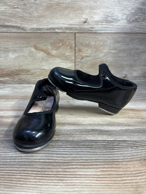 Black patent leather tap shoes with elastic straps on wood floor, Capezio brand