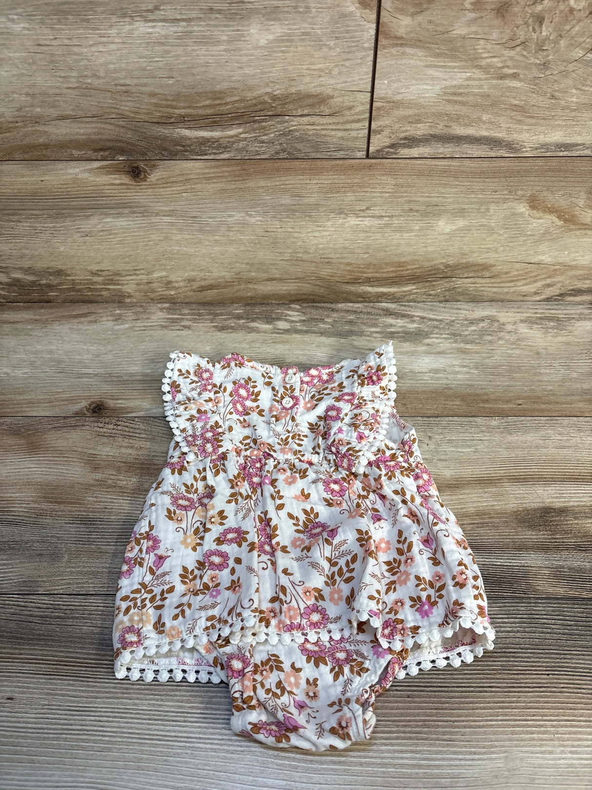 Top-down view of ivory Daisy Fuentes floral bodysuit dress 18M with pink and brown flowers, lace trim and attached bloomers on wood floor
