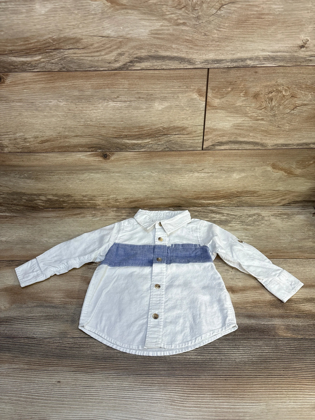 White long sleeve kids shirt with blue stripe and buttons, laid on wood surface