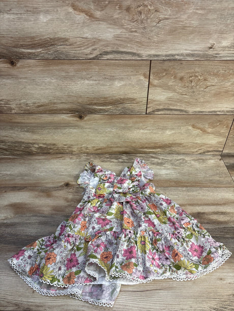 Flat lay of toddler floral dress with ruffle sleeves, front bow, tiered skirt and lace trim on wood floor