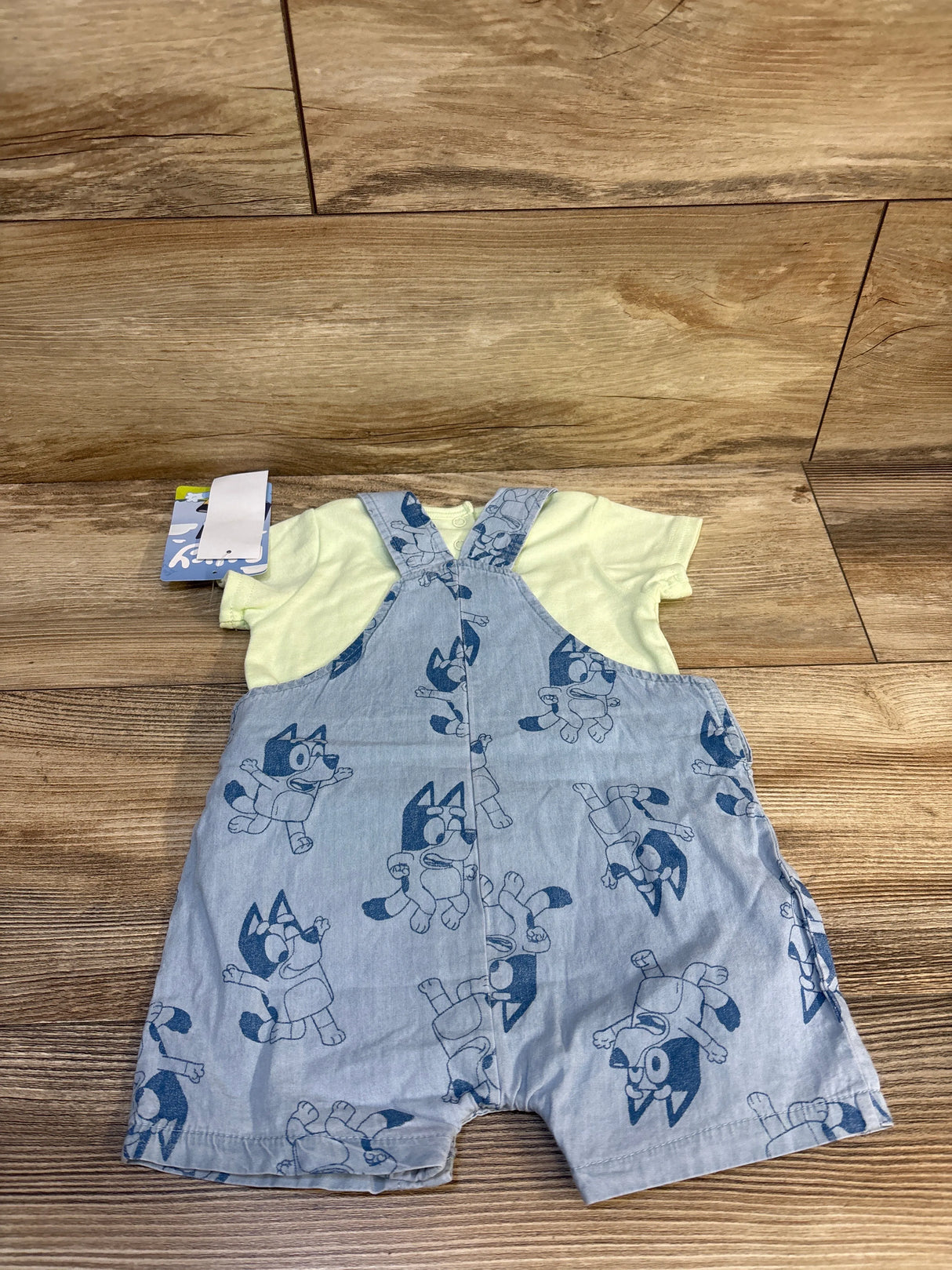 Baby outfit with yellow shirt and blue cartoon dog print overalls on wood floor