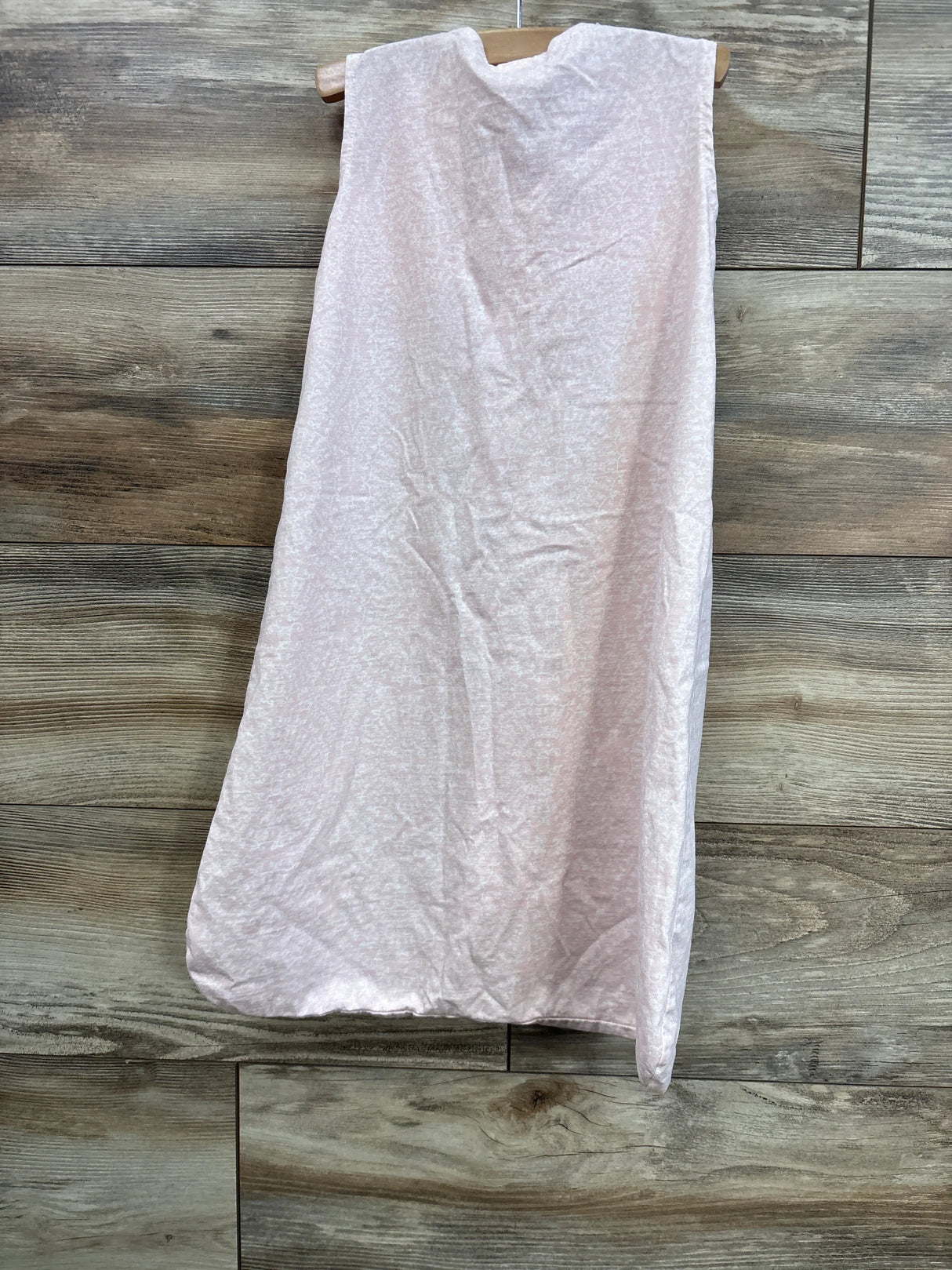 Front view of Yoga Sprout sleep sack in light pink, size 0–6M, sleeveless with roomy bottom, hanging on a wood plank background
