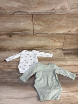 Top-down view of two newborn organic long-sleeve bodysuits, one sage green and one white with green apple print, on wood floor