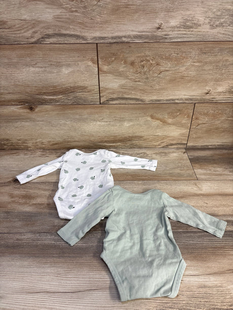 Top-down view of two newborn organic long-sleeve bodysuits, one sage green and one white with green apple print, on wood floor