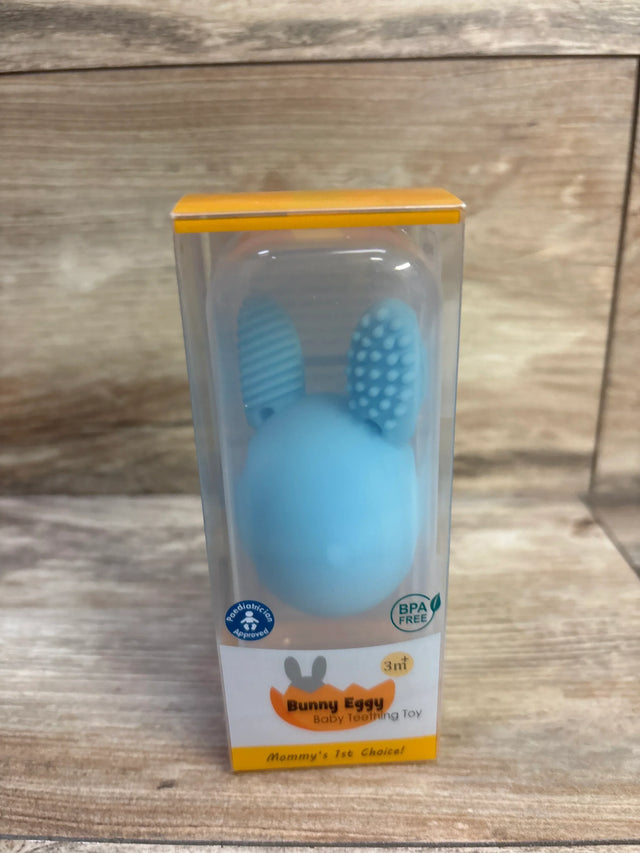 Front view of blue Bunny Egg teether in clear box showing textured rabbit ears and BPA free label on wooden tabletop