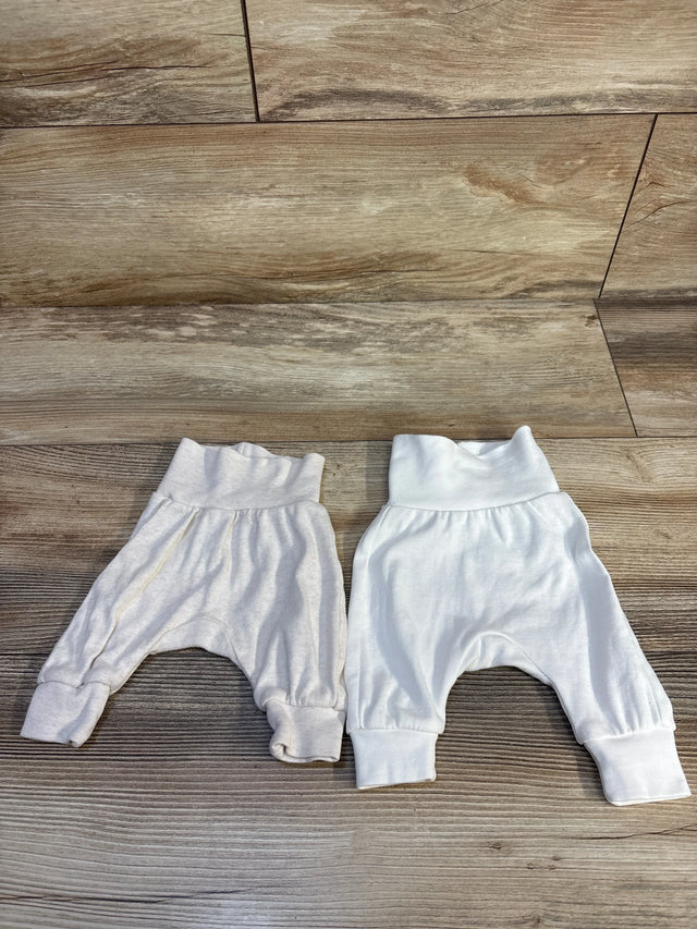 Two pairs of baby harem pants, white and off-white, laid flat on wood floor for resale