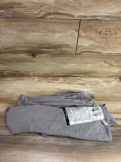 Top view of grey Moby Ring Sling Baby Carrier folded to show metal rings and a warning label on wood flooring
