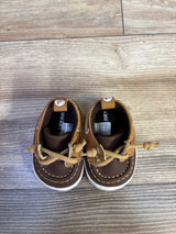 Top-down view of Sperry brown and tan boat crib shoes size 2C showcasing tied laces and white rubber soles on wood floor