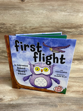 Children's book titled 'First Flight' with cartoon owls on purple cover, displayed on wooden surface