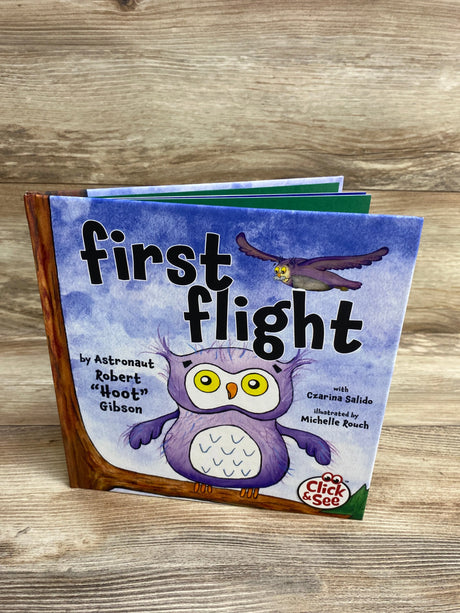 Children's book titled 'First Flight' with cartoon owls on purple cover, displayed on wooden surface