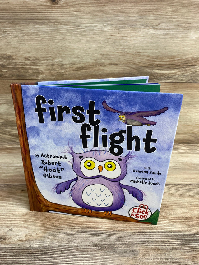 Children's book titled 'First Flight' with cartoon owls on purple cover, displayed on wooden surface