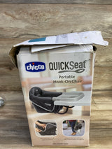 Front view of Chicco QuickSeat portable hook-on chair box showing dark gray hook-on chair with detachable tray against a wooden backdrop