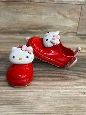 Front view of Mini Melissa Hello Kitty red slip-on toddler shoes showing white Hello Kitty face charms with pink bows on wood floor