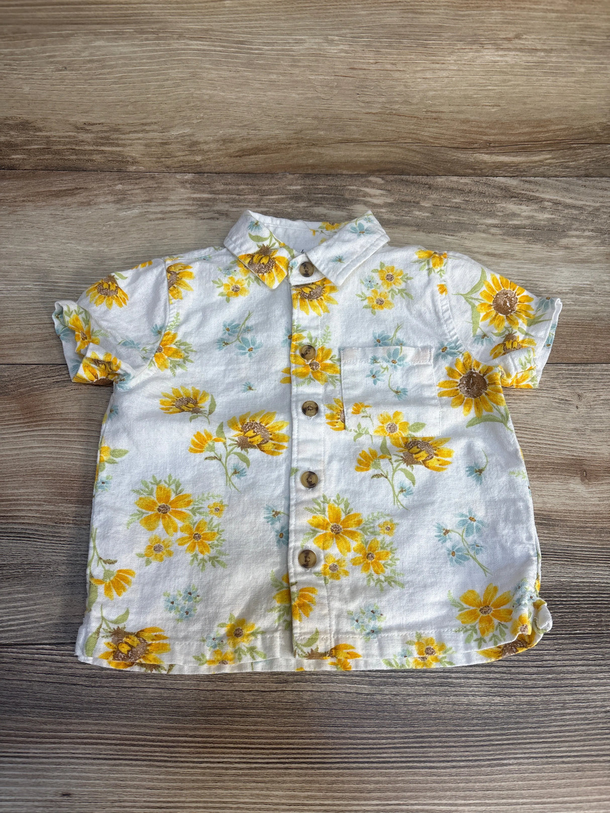 Short sleeve baby shirt with yellow floral print and buttons on wood background