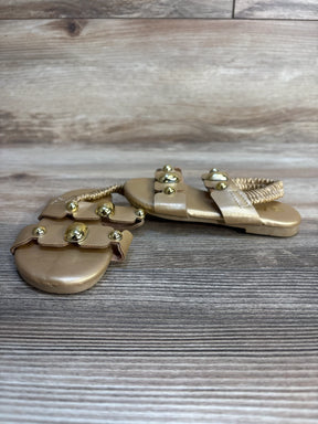 Gold toddler sandals with elastic ankle strap and decorative studs on wood background
